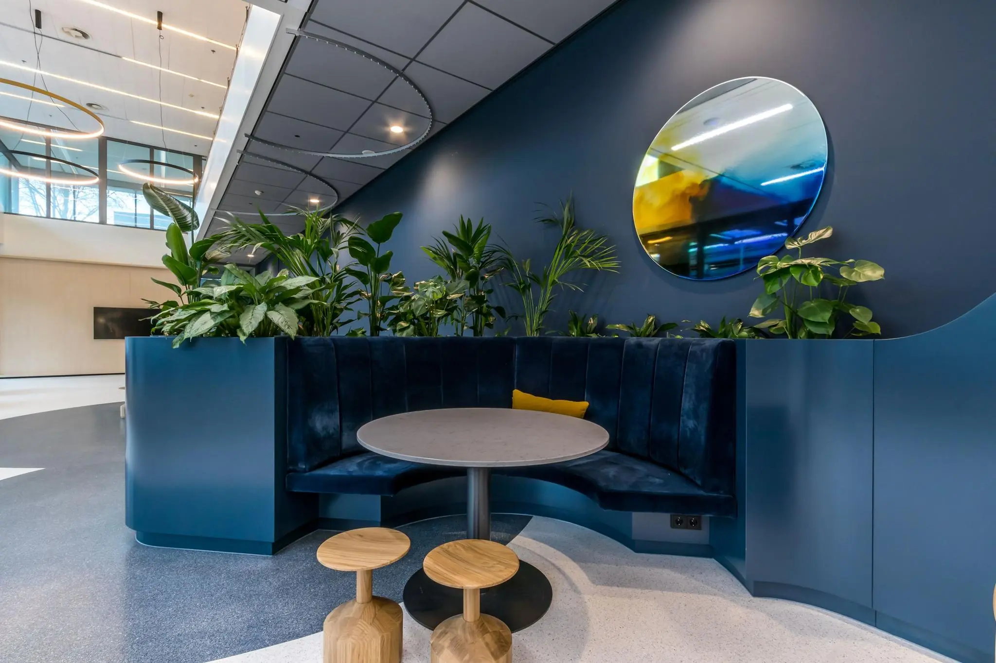 Moderne zithoek op Vliegend Hertlaan met ronde bank, plantenwand en gekleurd kunstwerk aan de muur.